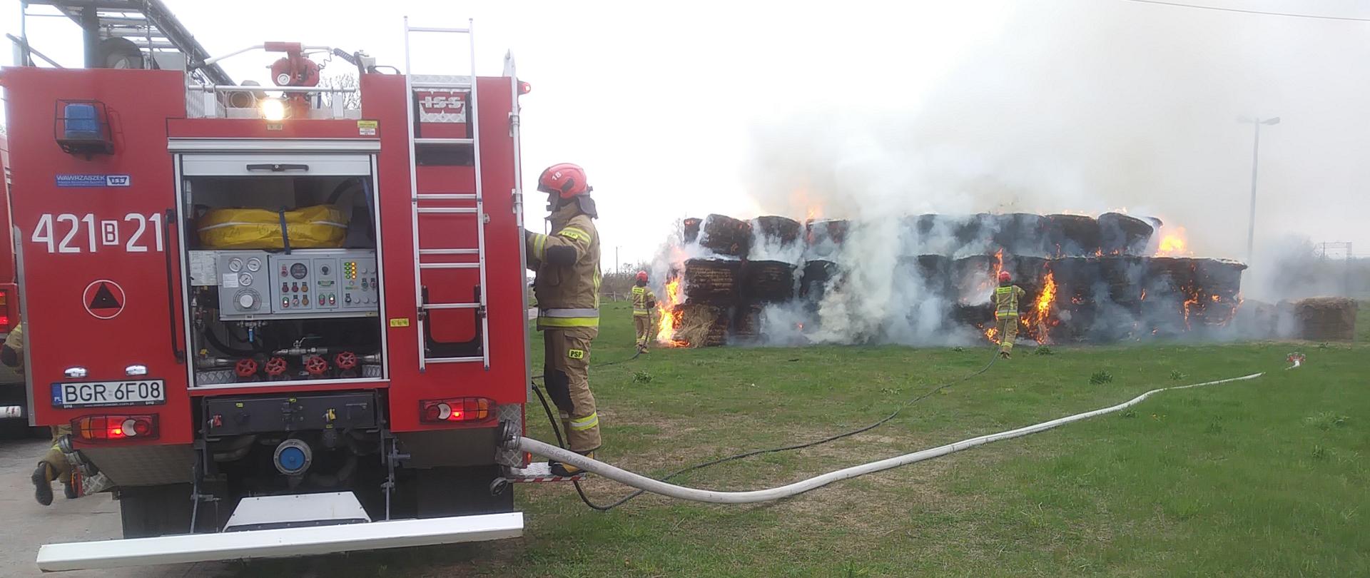 Pojazd gaśniczy PSP z podpiętą linią gaśniczą. W tle paląca się sterta bel siana.