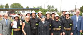 Dowódca zwycięskiej drużyny OSP z Silnicy prezentuje puchar i dyplom. Pozostali strażacy stoją w rzędzie. Wraz ze strażakami do zdjęcia pozują osoby wręczające nagrody/ puchary.