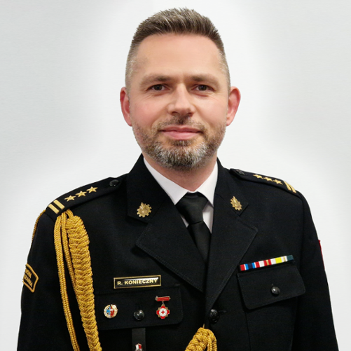 Zdjęcie przedstawia st. bryg. Rafała Koniecznego Zastępce Lubuskiego Komendanta Wojewódzkiego PSP w Gorzowie Wlkp. w mundurze na szarym tle.