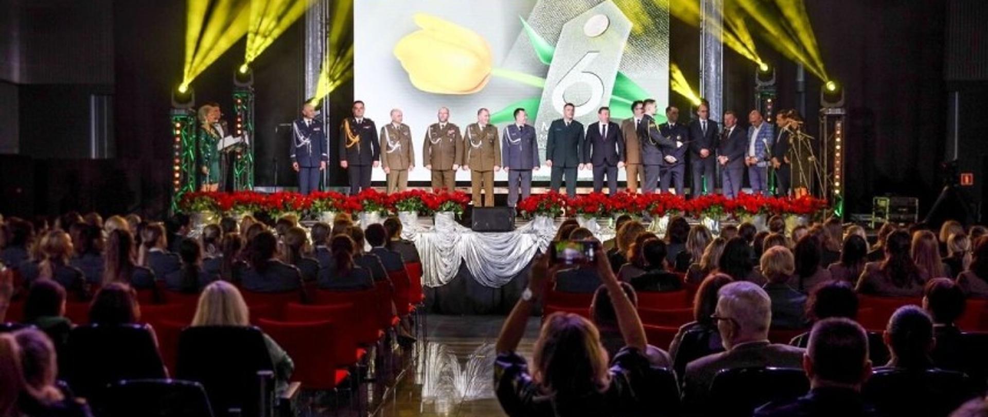 Zdjęcie przedstawia Salę Konferencyjną Targów Kielce. Na scenie przedstawiciele służb mundurowych składający życzenia paniom. Poniżej siedzą uczestnicy gali.