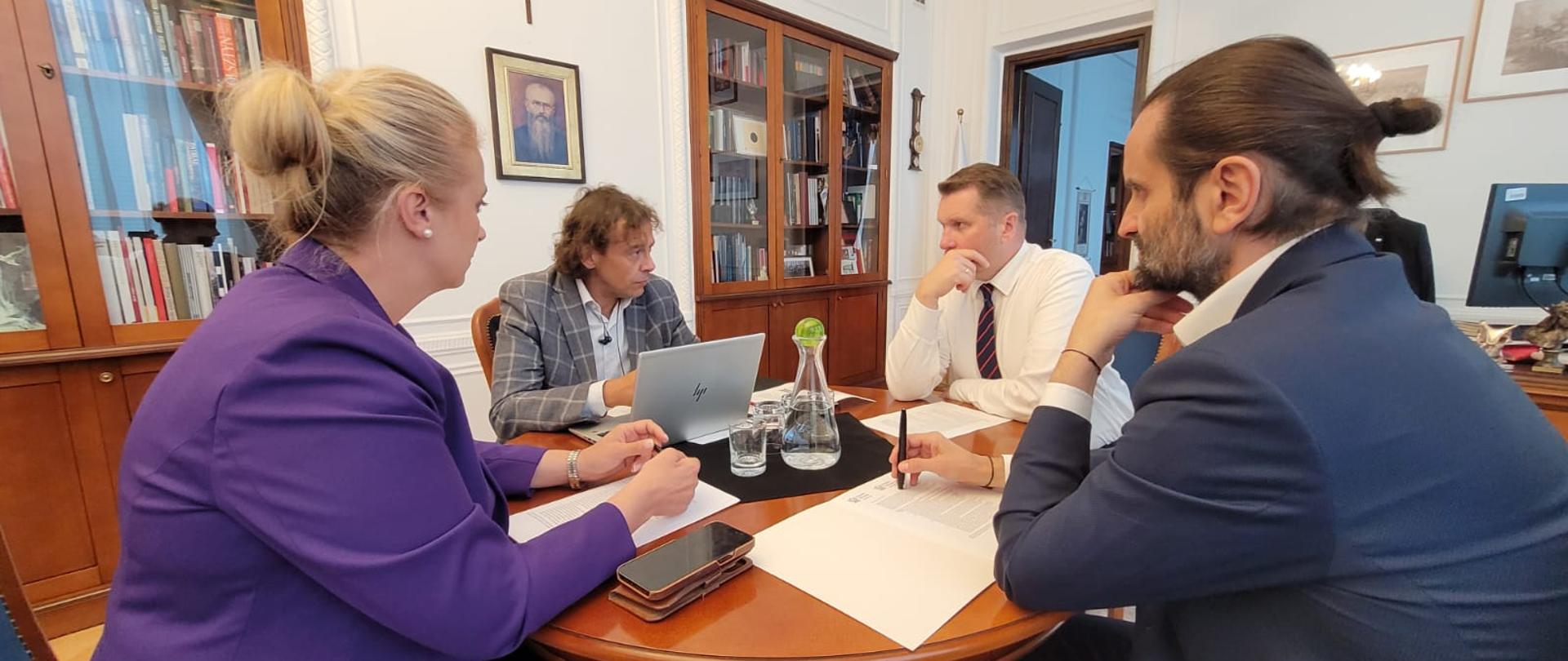 Przy okrągłym stoliku siedzi minister Czarnek i trzy osoby, przed nimi dokumenty i otwarty laptop.