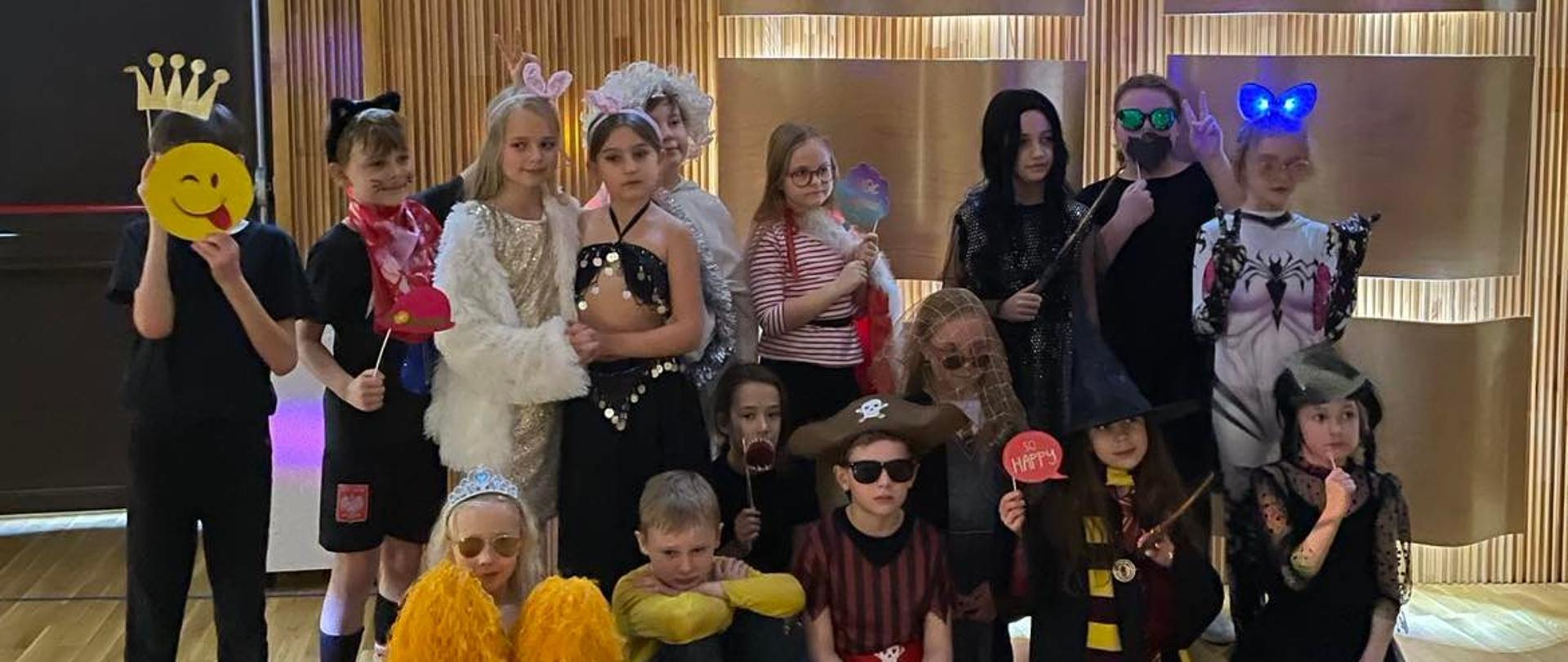 Zdjęcie przebranych dzieci w czasie balu karnawałowego na tle paneli w sali koncertowej.
