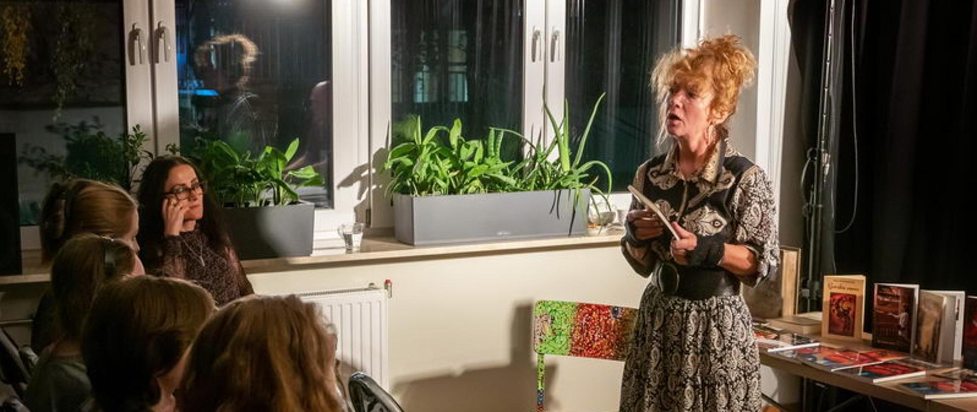 zdjęcie przedstawia naszego gościa - poetkę recytującą wiersze, w tle okno i stolik na którym stoją książki naszej poetki