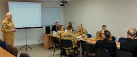 Kilkunastu strażaków siedzi przy stołach w świetlicy. Na wprost prezentację multimedialną omawia Komendant Powiatowy PSP w Rypinie starszy brygadier Grzegorz Łydkowski.