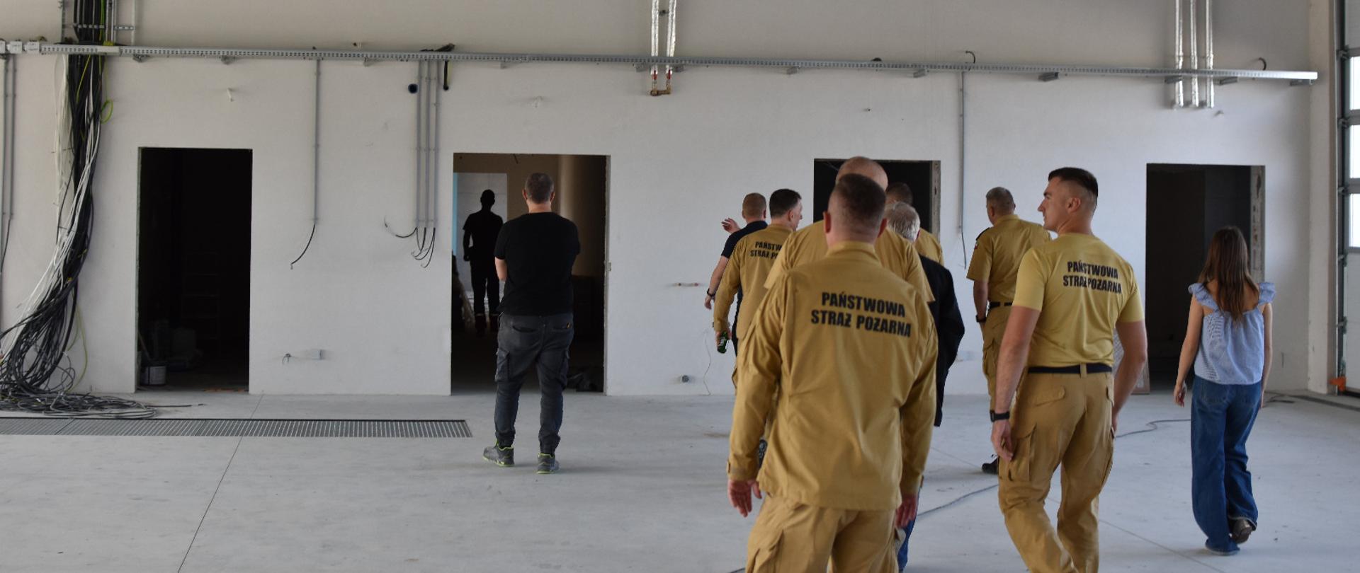Na zdjęciu grupa kilkunastu osób ogląda wnętrze budynku w stanie surowym. Większość grupy stanowią funkcjonariusze Państwowej Straży Pożarnej. Wszyscy są odwróceni tyłem od fotografującego. 