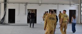 Na zdjęciu grupa kilkunastu osób ogląda wnętrze budynku w stanie surowym. Większość grupy stanowią funkcjonariusze Państwowej Straży Pożarnej. Wszyscy są odwróceni tyłem od fotografującego. 