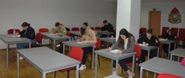 Świetlica komendy. Przy stolikach siedzą uczestnicy eliminacji, którzy rozwiązuja test pisemny. W tle ściana z logo PSP.