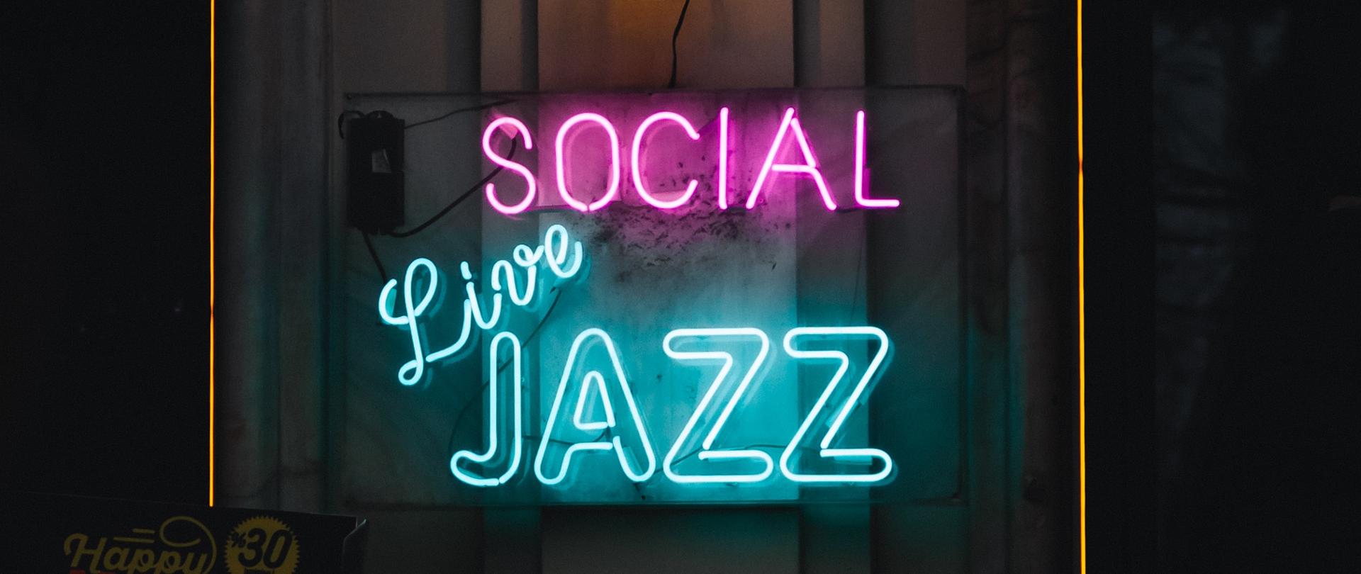 w centralnej części neonowy napis w języku angielski social live jazz całość na ciemnym tle