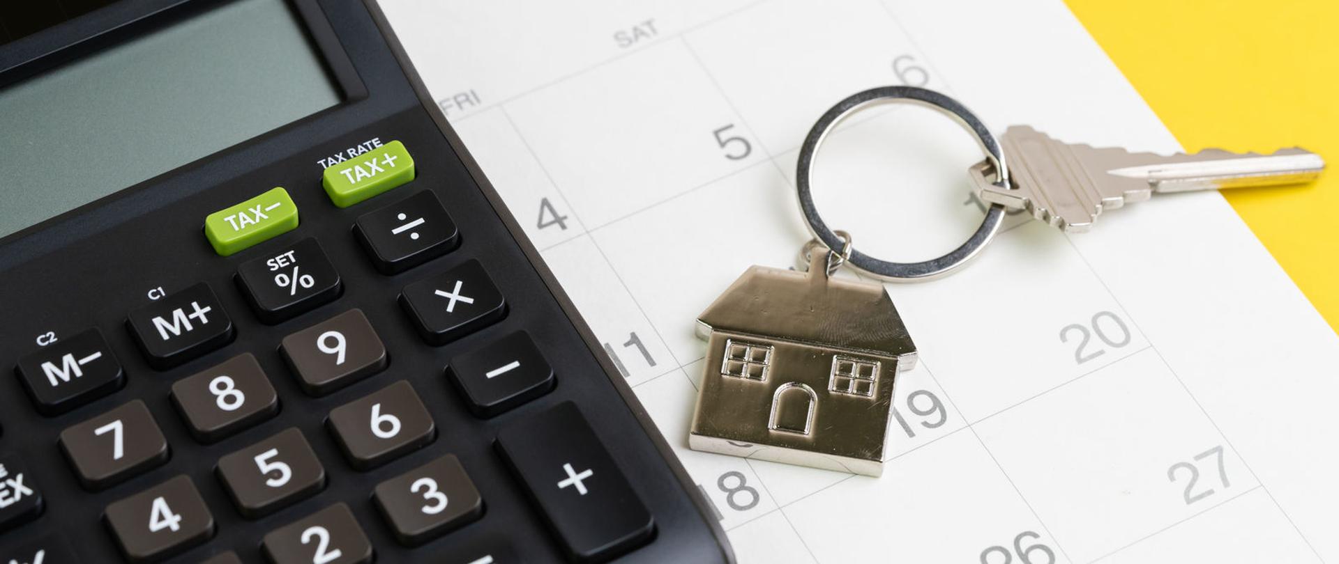 Kalkulator i klucz z brelokiem w kształcie domu na kalendarzu.