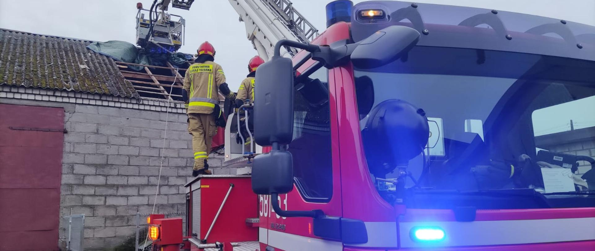 samochód strażacki podnośnik koszowy rozstawiony przy budynku gospodarczym z którego zostały zerwane płyty eternitu