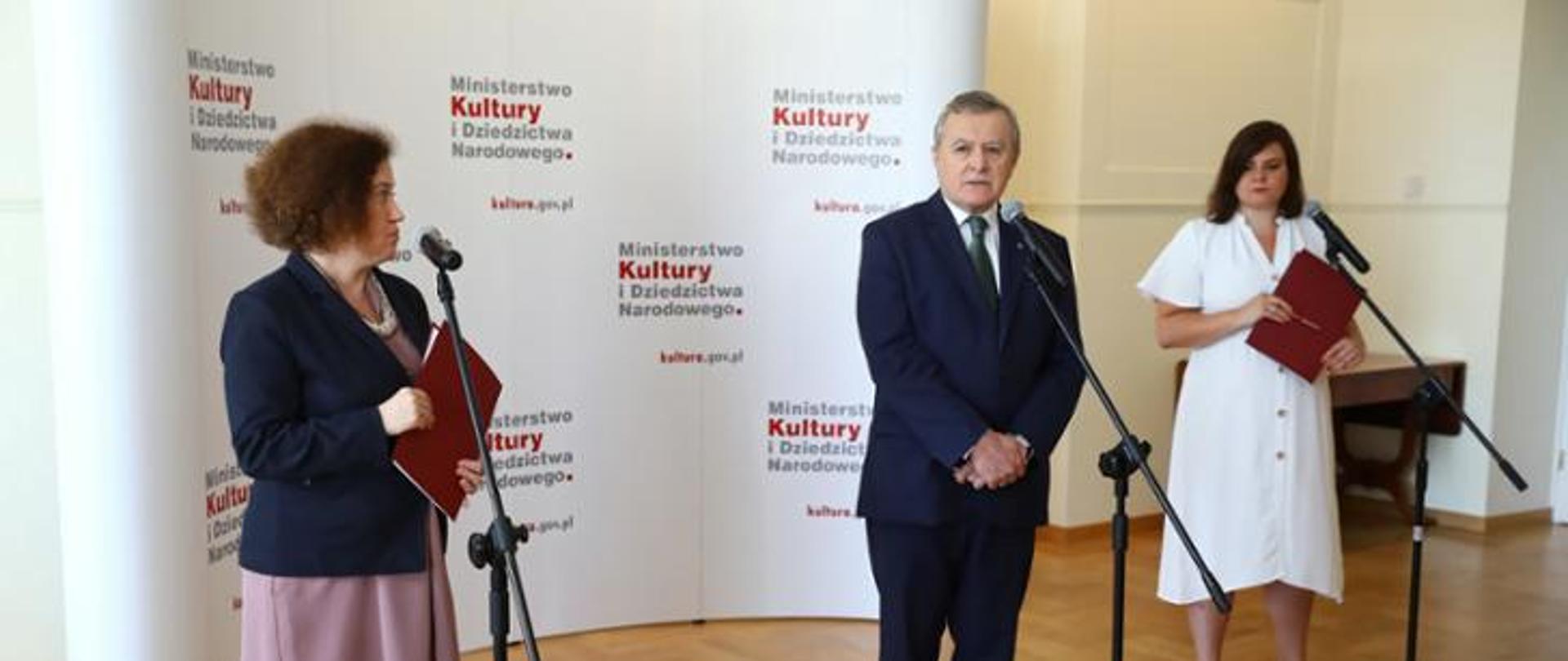 Biały baner z napisem Ministerstwo Kultury i Dziedzictwa Narodowego. Obrazek konferencji prasowej.