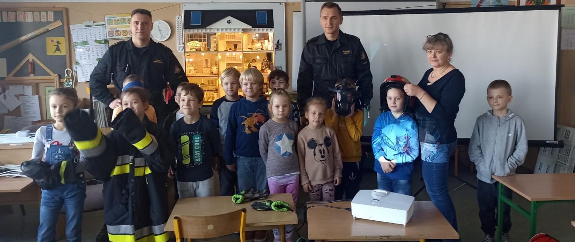 Na zdjęciu znajdują się funkcjonariusze oraz dzieci na tle mobilnego symulatora zagrożeń pożarowych, zdjęcie wykonano w jednej z klas Zespołu Szkół w Unisławiu.