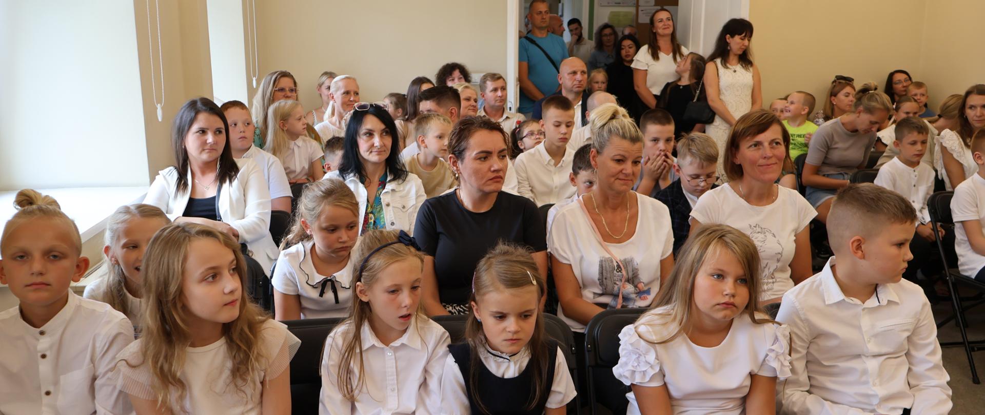 Uczniowie i rodzice siedzący w auli szkoły.