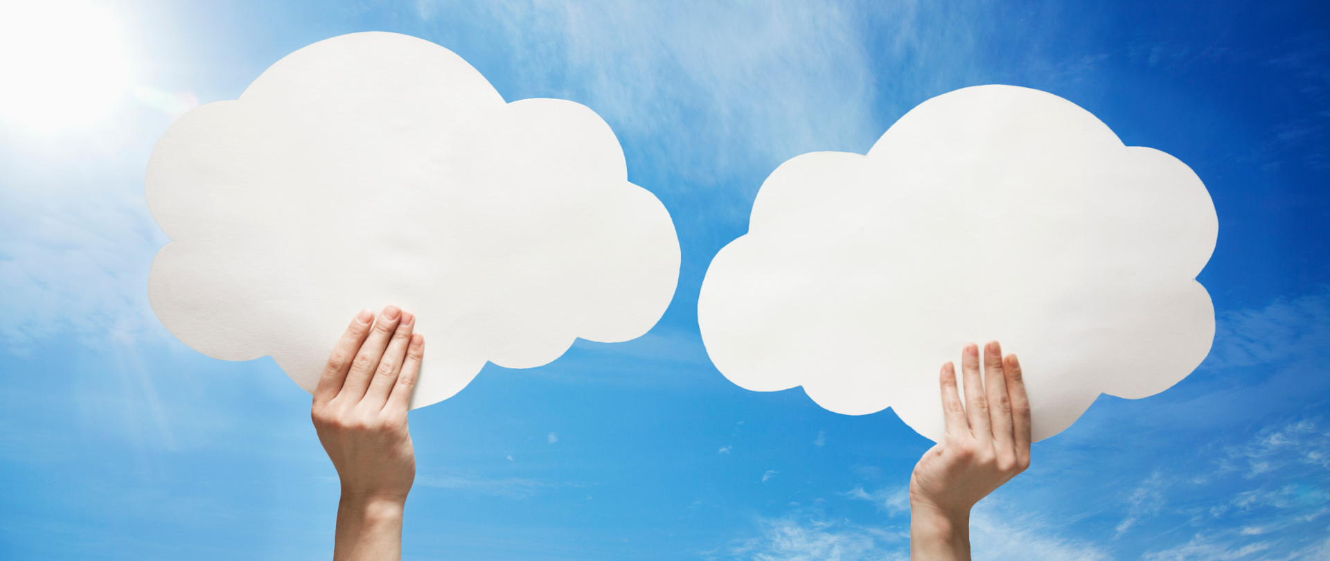 Dwie uniesione ręce trzymające papierowo chmury na tle błękitnego nieba