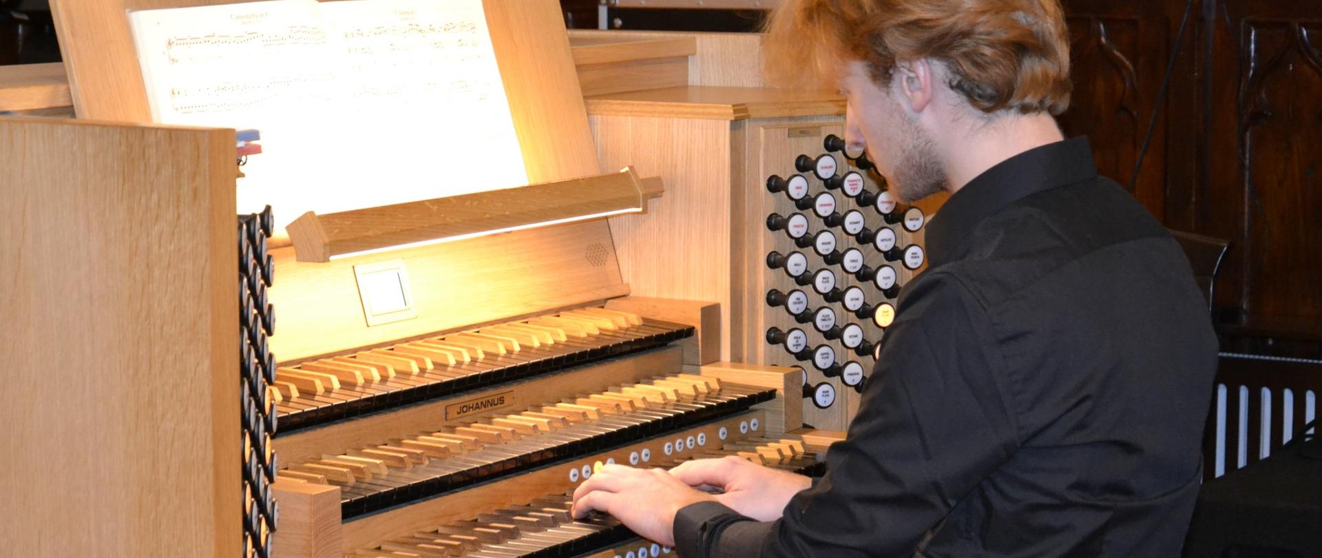 zdjęcie przedstawia Dominika Kapinosa siedzącego przy szkolnych organach w kolorze jasnego drzewa