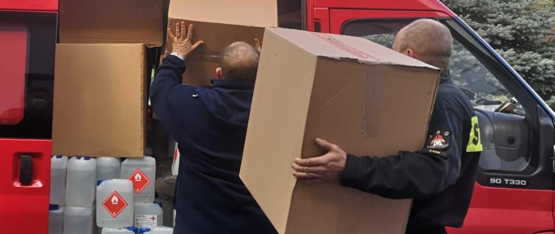 Zdjęcie przedstawia dwóch strażaków przygotowujących transport maseczek ochronnych