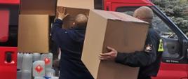 Zdjęcie przedstawia dwóch strażaków przygotowujących transport maseczek ochronnych