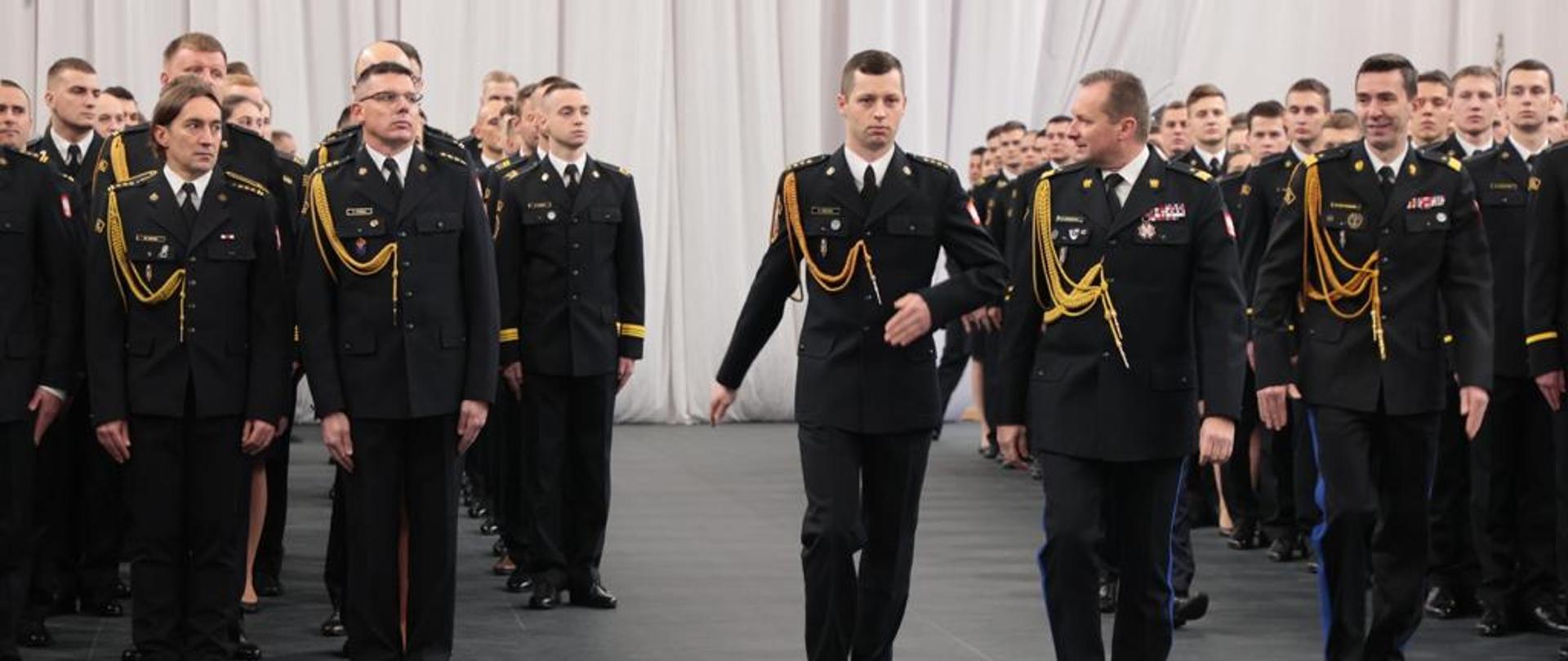 Z-ca KG PSP maszeruje wraz z rektorem szkoły przez środek sali, po lewej i prawej ustawieni są podchorążowie SGSP