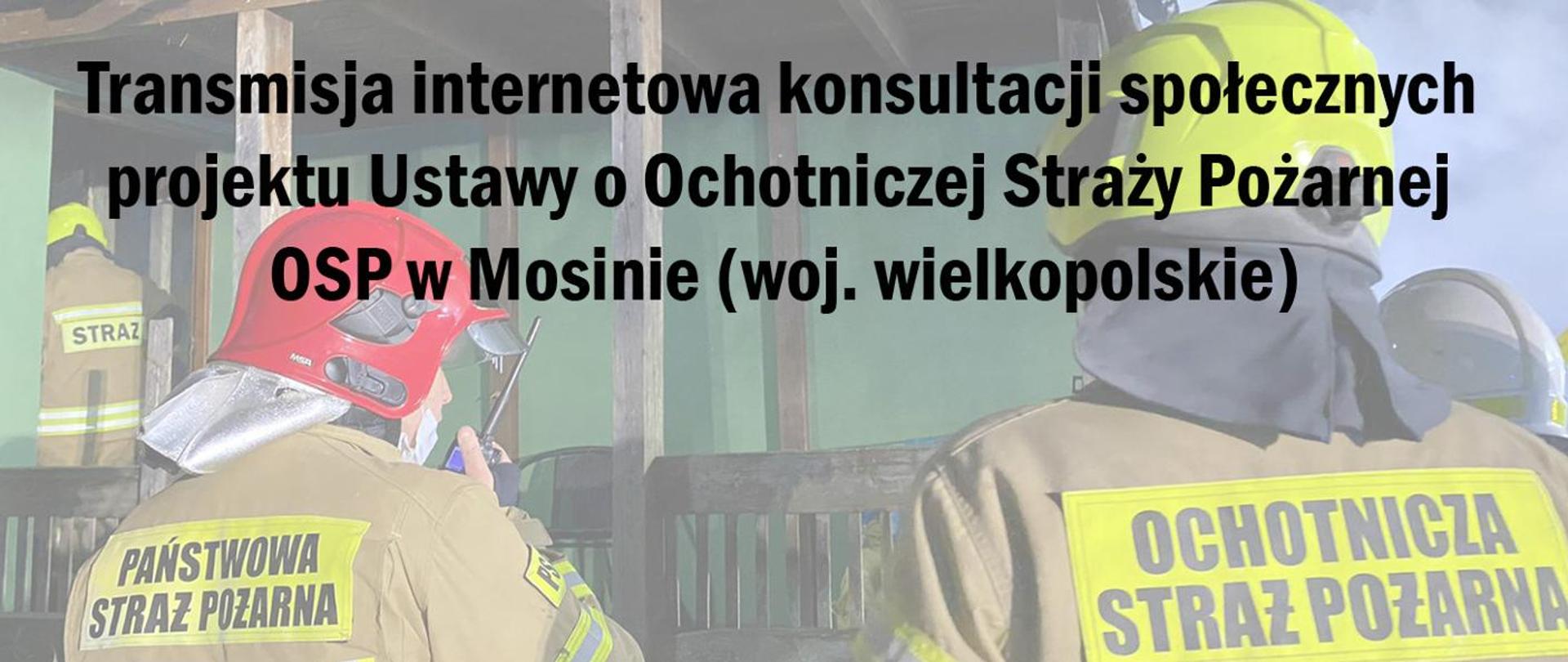 Stojący tyłem funkcjonariusz Państwowej Straży Pożarnej oraz przedstawiciel Ochotniczej Straży pożarnej - oboje stoją tyłem ubrani w ubrania specjalne w kolorze piaskowym (żółtym). Funkcjonariusz PSP podaje informacje przez radiostację trzymaną w prawej ręce. Zdjęcie wykonano na tle ściany zabudowania.