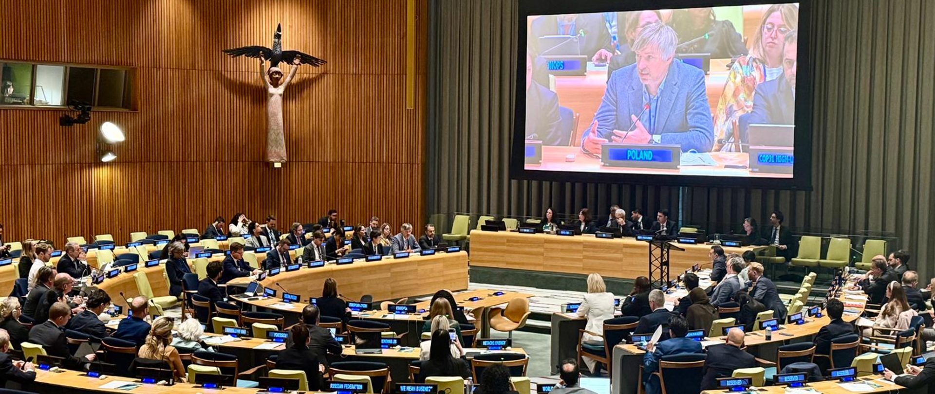 Deputy Minister of Climate and Environment Krzysztof Bolesta during the 81st session of the UN General Assembly in New York. The photograph shows a broadcast of the Deputy Minister’s remarks on a large screen in the centre of the conference room. Numerous seats occupied by other participants in the session are visible.