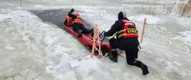 Strażacy przeprowadzają ćwiczenia z ratownictwa lodowego na zamarzniętym zalewie przy użyciu sań ratunkowych. Ratownik wyciąga pozoranta z przerębla na bezpieczną taflę lodu w wyznaczonym i zabezpieczonym sektorze.