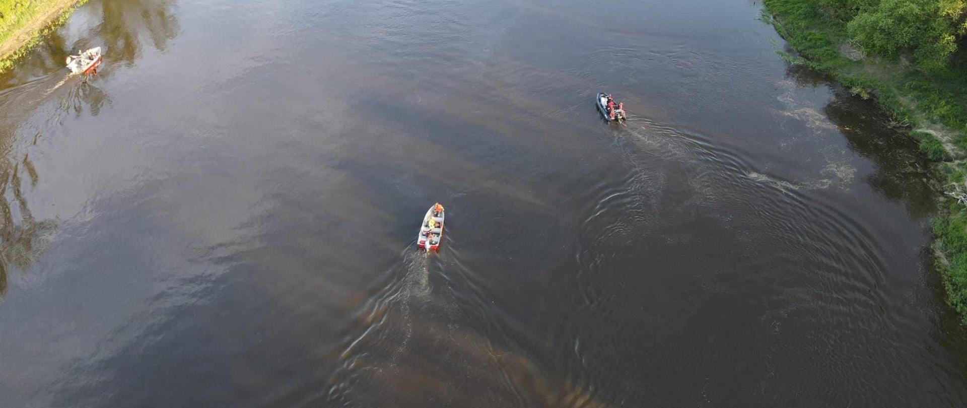 Widać rzekę Bug a na niej pływające łódki poszukujące osób zaginionych w wodzie 