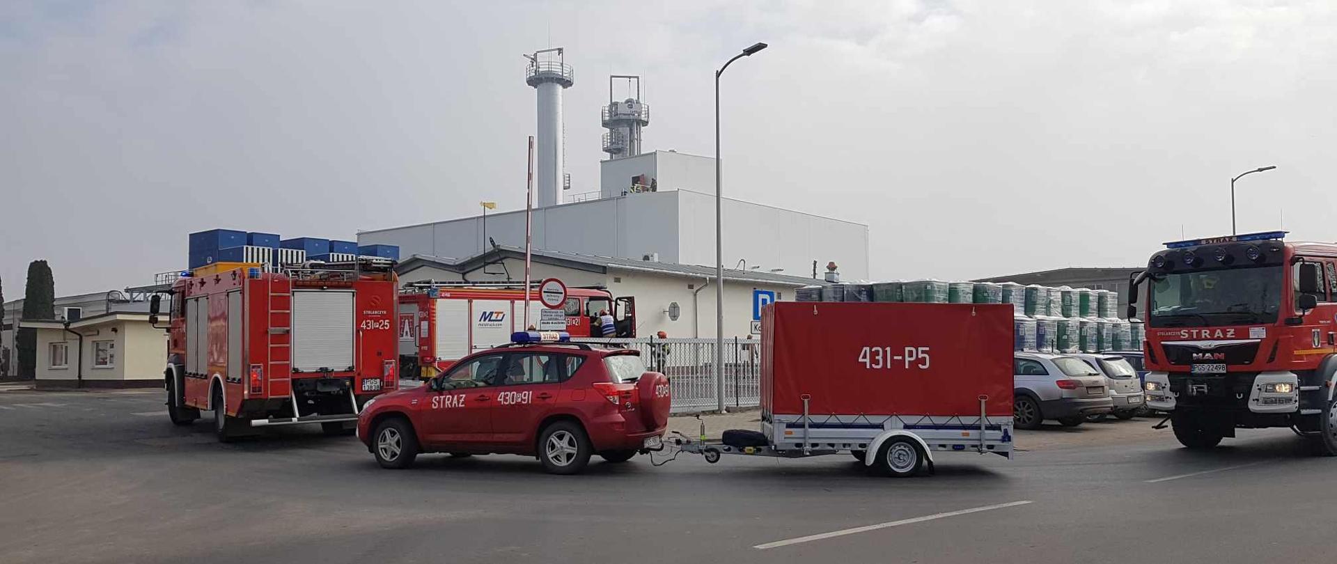Wozy strażackie wjeżdżające na teren zakładu. Jeden z nich ciągnie za sobą przyczepkę chemiczną. 