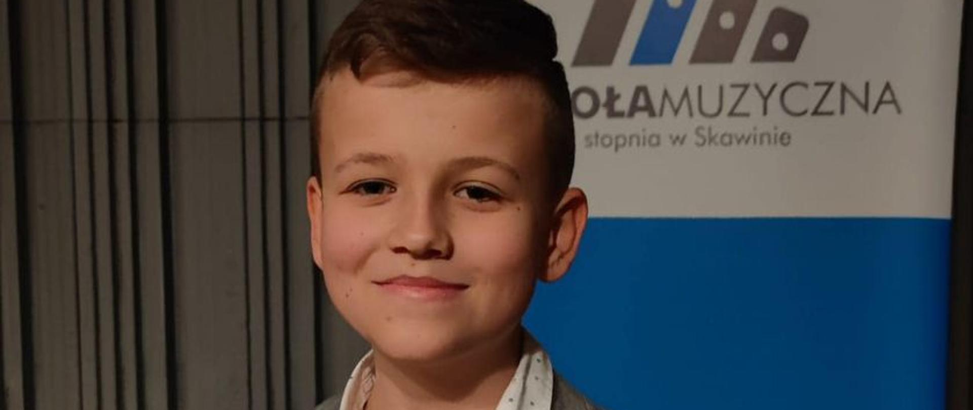 Zdjęcie przedstawia uśmiechniętego chłopca trzymającego w ręku dyplom z konkursu