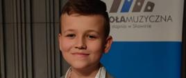 Zdjęcie przedstawia uśmiechniętego chłopca trzymającego w ręku dyplom z konkursu