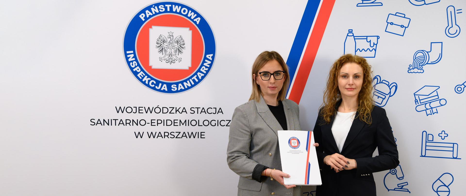 Magdalena Kaczmarek, Mazowiecki Państwowy Wojewódzki Inspektor Sanitarny i Justyna Szatkowska, nowy Państwowy Powiatowy Inspektor Sanitarny w Płocku stoją razem na tle ścianki reklamowej z logo PIS