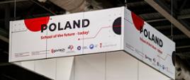 Widok na sufit hali, pod sufitem wisi biały czworokąt na którego ściankach są napisy Poland - school of the future today.