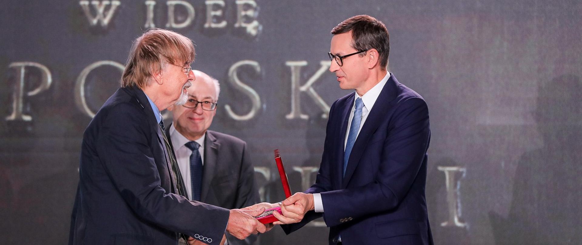 Premier ściska dłoń odznaczonego medalem mężczyzny.