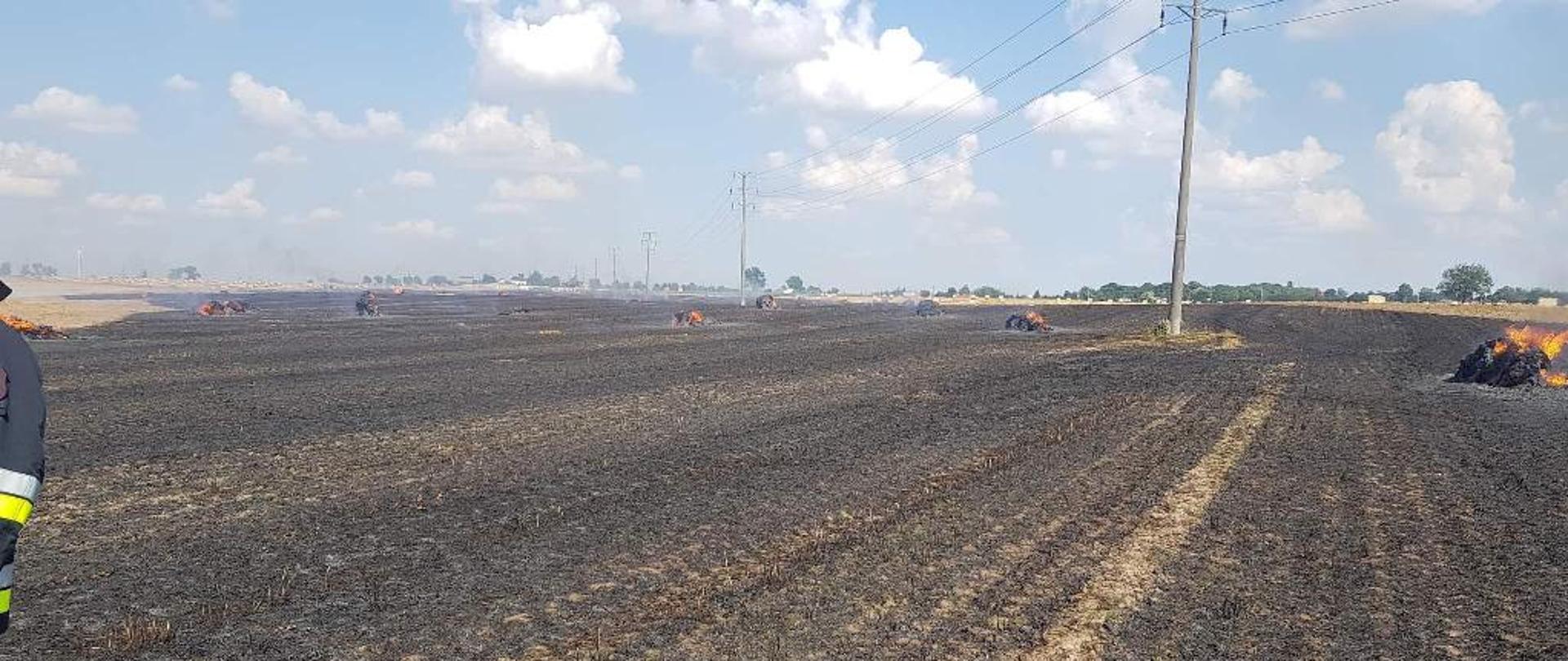 Pożar ścierniska na polu, w oddali widać kilka palących się balotów słomy