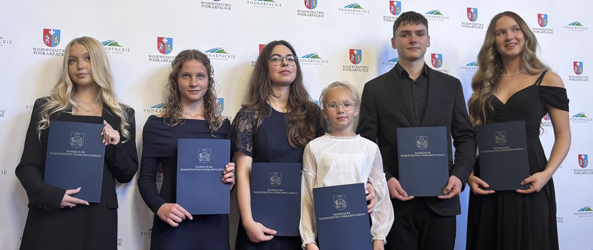 Laureaci stypendiów "Nie zagubić talentu". Laureaci na tle baneru z logami organizatorów.