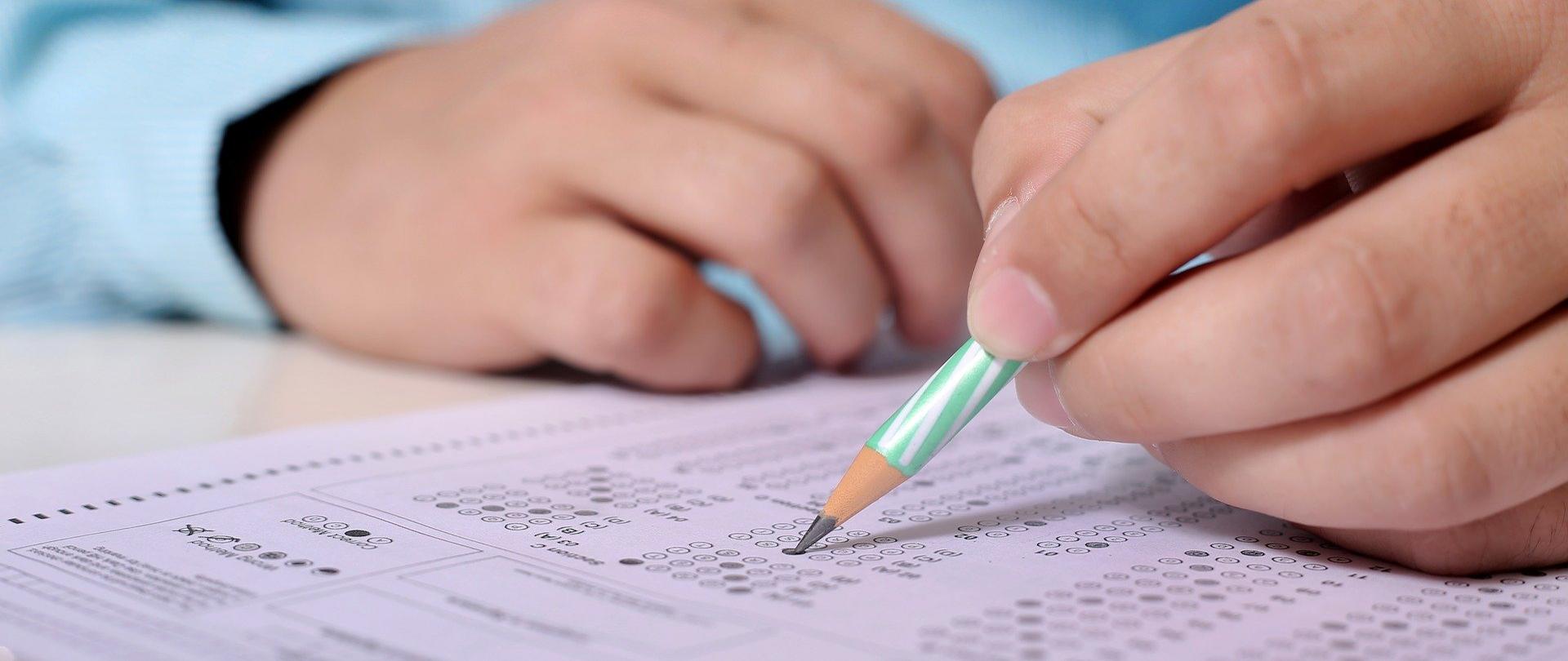 męskie dłonie, człowiek ubrany w błękitną koszulę w jednej ręce trzyma ołówek, którym wypełnia test
