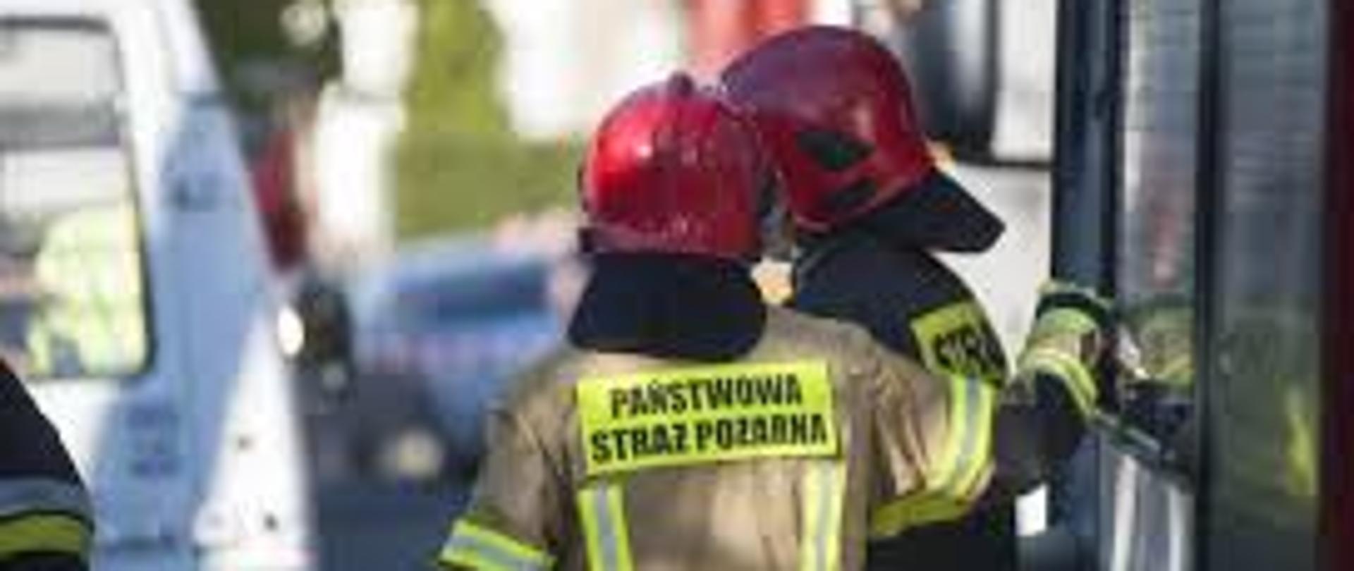 Zdjęcie przedstawia dwóch strażaków przy wozie bojowym.