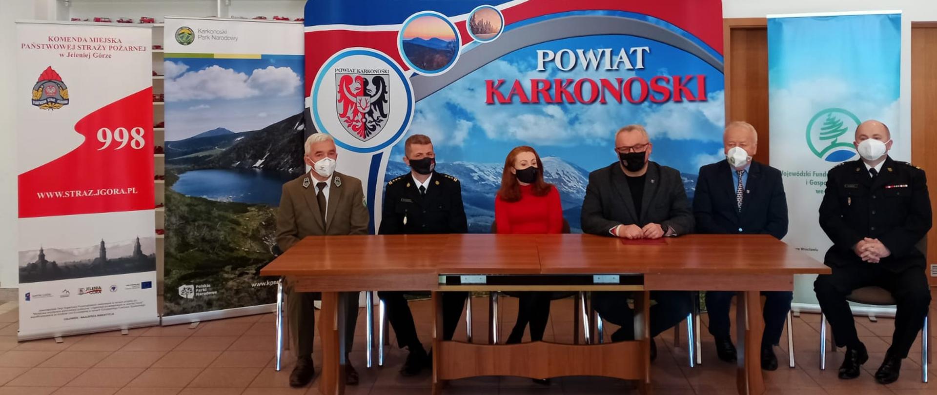 Zdjęcie przedstawia przedstawicieli podmiotów zaangażowanych w projekt. Sześć osób siedzi przy stole prezydialnym, a za nimi są rollupy reklamujące instytucje.