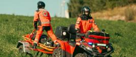 Na zdjęciu widoczni są ratownicy na quadzie wraz z przyczepką w trakcie transportu osoby poszkodowanej.