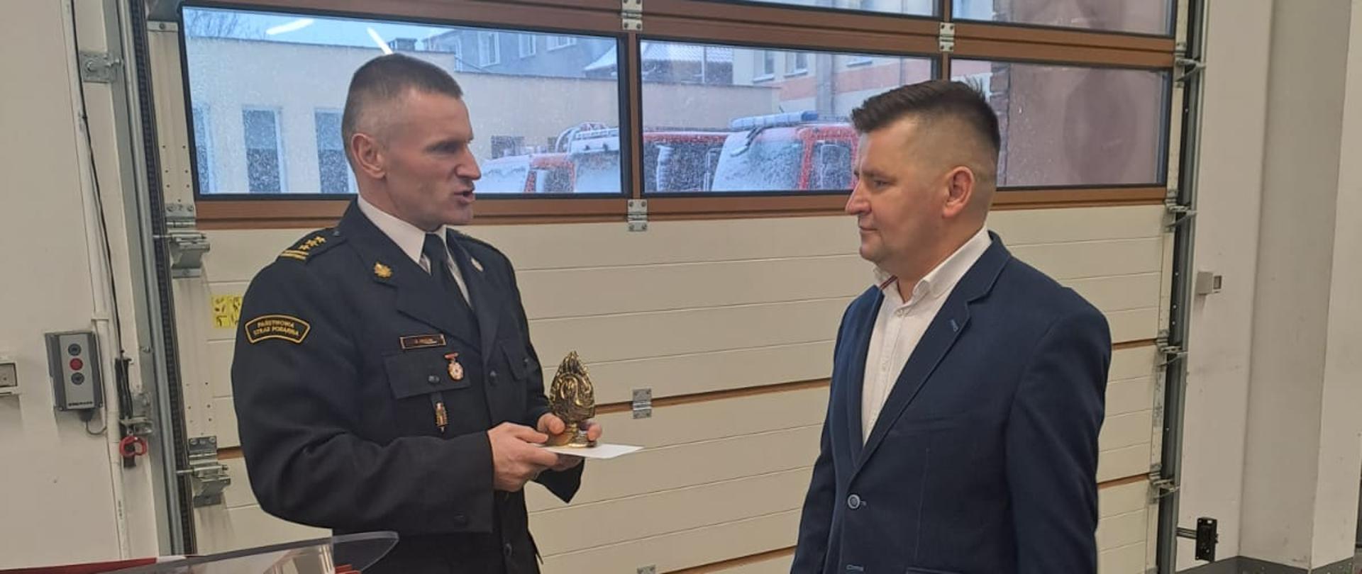 Na zdjęciu widać komendanta powiatowego, który wręcza statuetkę odchodzącemu na emeryturę strażakowi.