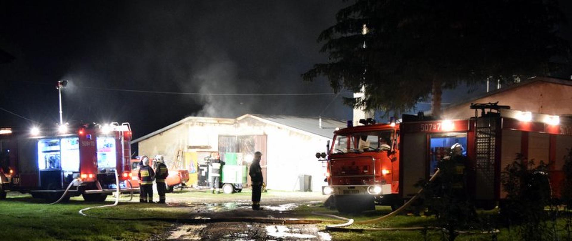 Zdjęcie przedstawia działania ratowniczo gaśnicze gaszenia dużego pożaru fermy drobiu w porze nocnej w miejscowości Żarówka. Na tle palącego się kurnika stoją samochody ratowniczo gaśnicze jednostek Państwowej Straży Pożarnej i Ochotniczej Straży Pożarnej.