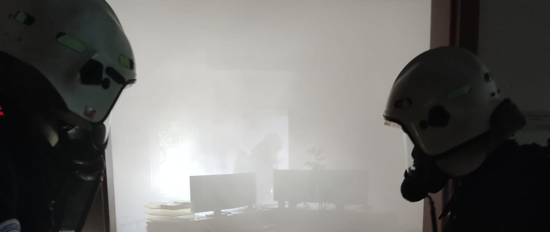 Dwóch strażaków OSP wchodzi do zadymionego pomieszczenia