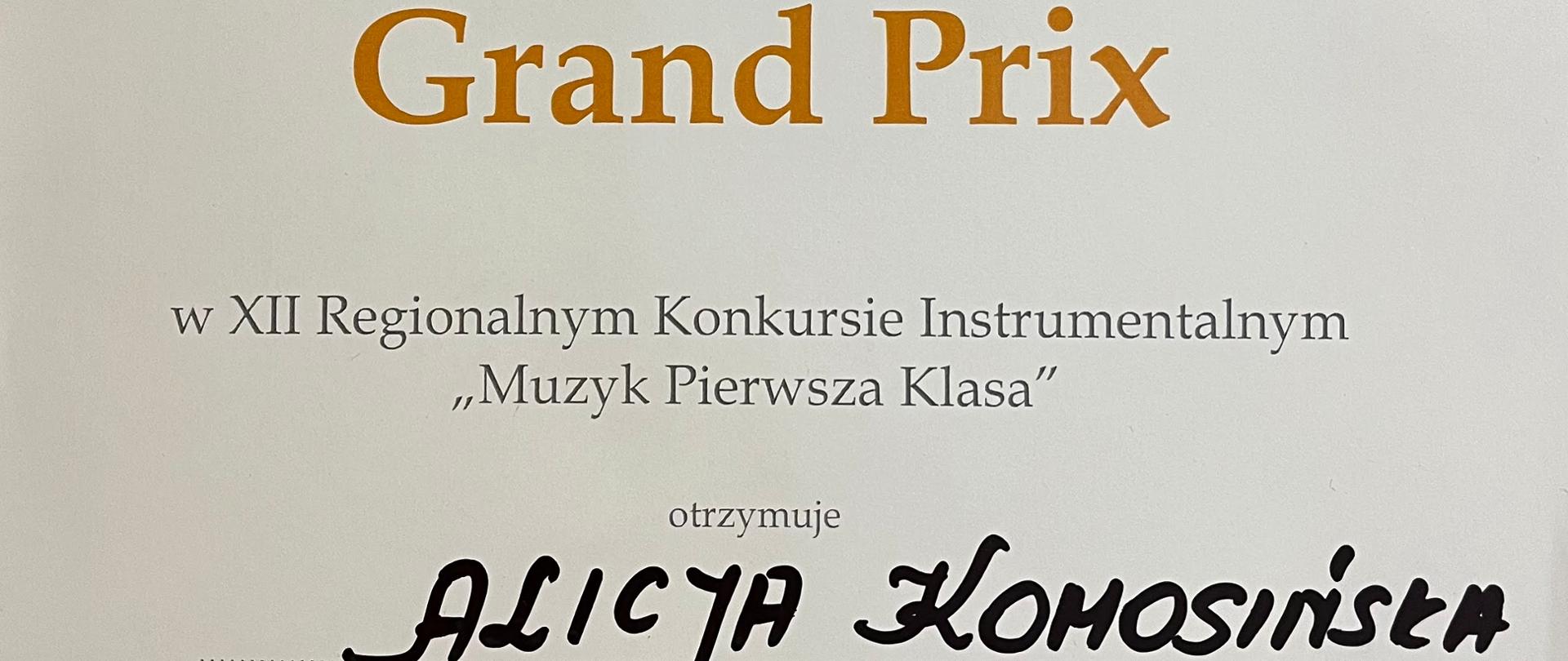 Na zdjęciu widać dyplom z nagrodą Grand Prix XII Regionalnego Konkursu Instrumentalnego "Muzyk pierwsza klasa". Dyplom jest utrzymany w tonacji koloru białego. W prawym górnym rogu widać grafikę drzewa oraz dziecka z futerałem do instrumentu.