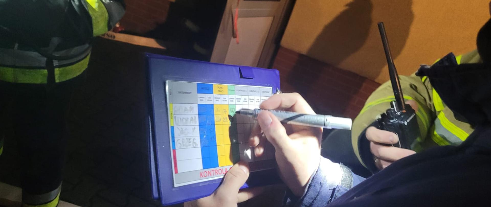 Zdjęcie ukazuje strażaka zapisującego na tablicy pomiary podczas ćwiczeń praktycznych