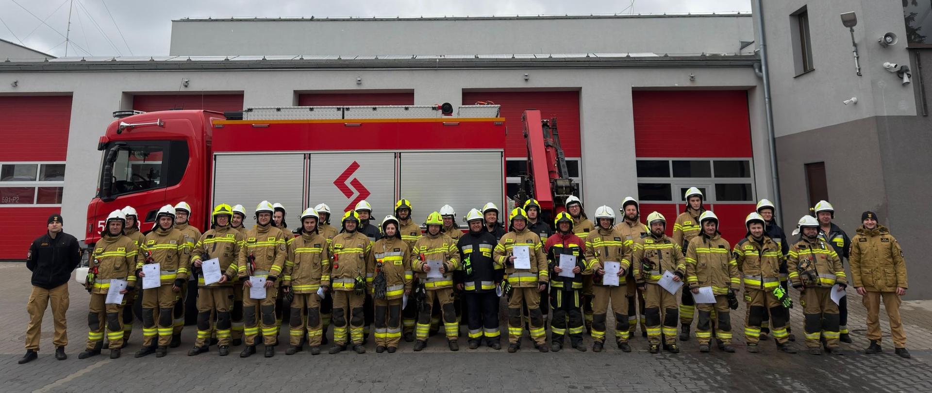 Strażacy na zdjęciu grupowym na tle samochodu i komendy
