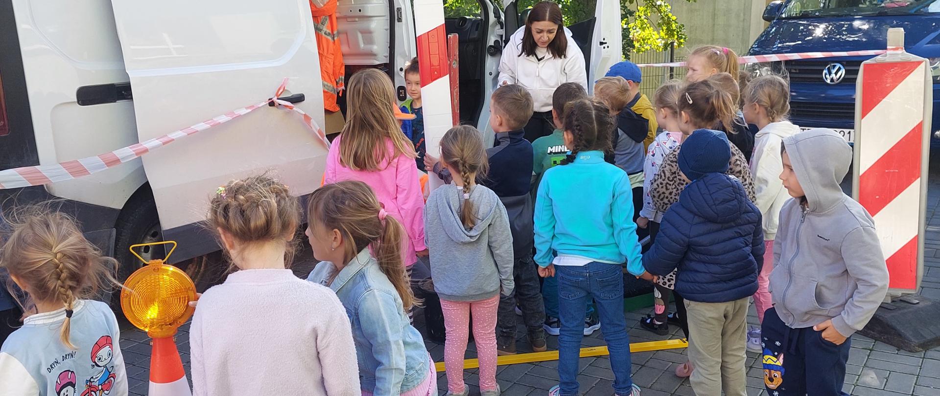 Dzień Budowlańca w przedszkolu - grupa dzieci przy samochodzie służby drogowej ogląda elementy oznakowania dróg 