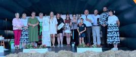 Na scenie znajduje się grupa osób-są to laureaci konkursu, który w rękach trzymają wygrane nagrody.
