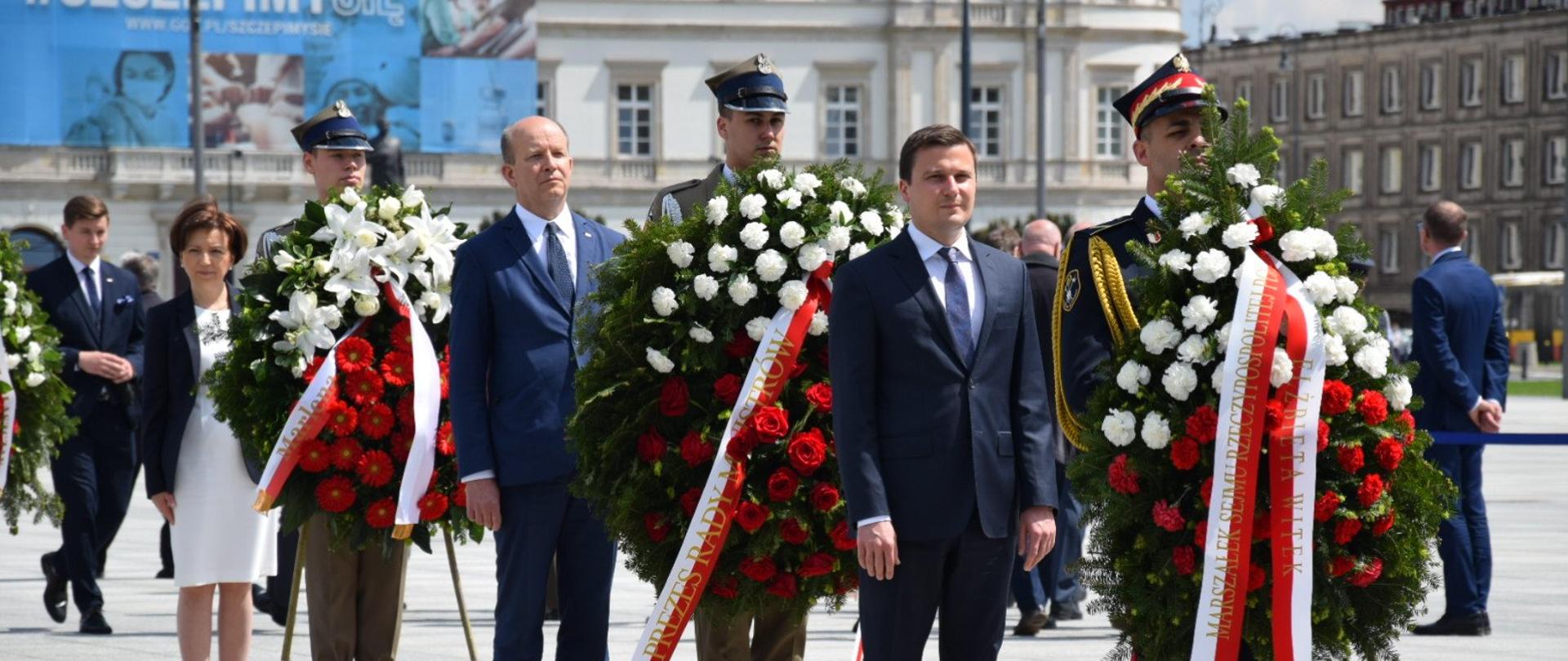 Moment złożenia wieńców przy Grobie Nieznanego Żołnierza na pl. Piłsudskiego w Warszawie. Na zdjęciu w rzędzie, jeden za drugim, stoją osoby składające wieńce. 
