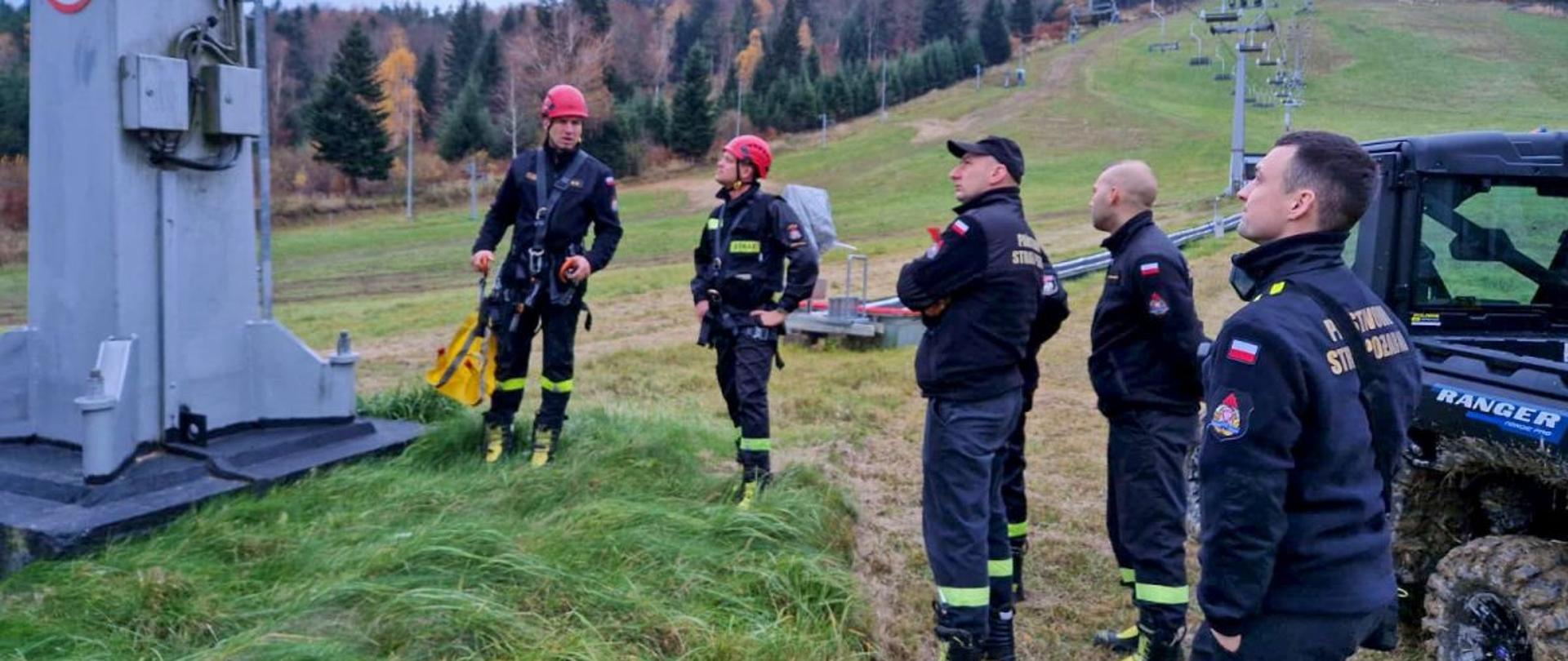 Zdjęcie przedstawia strażaków JRG, dwóch ze strażaków ubrana jest w sprzęt wysokościowy. Stoją przy podporze na wyciągu Laworta. Obok strażaków stoi pojazd polaris ranger. 