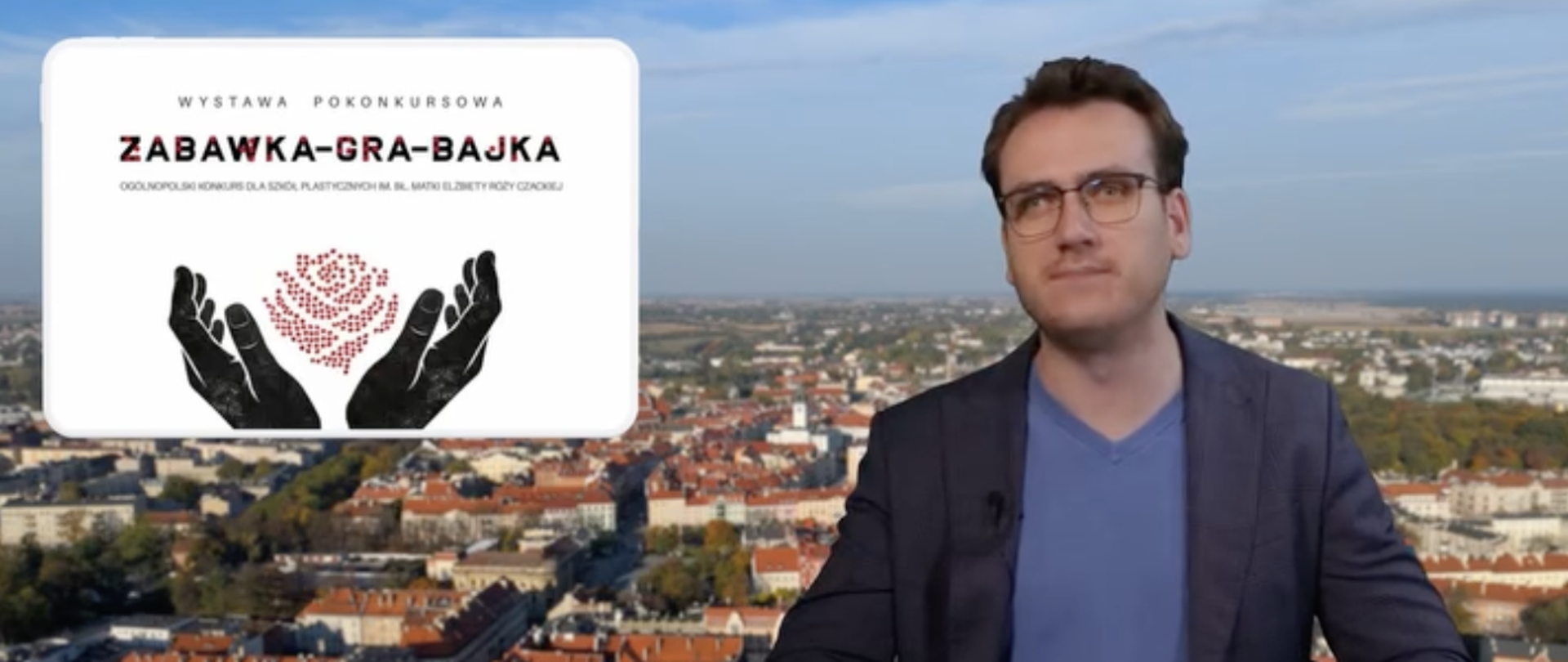 Mężczyzna w okularach - redaktor Telewizji Kalisz - siedzi z rekami na biurku, w ręce trzyma długopis, w tle widoczna jest panorama miasta Kalisza. W lewym górnym rogu widoczny jest plakat wystawy pokonkursowej ogólnopolskiego konkursu plastycznego pt. zabawka – gra - bajka z logo konkursu - dwoma dłońmi otaczającymi czerwoną, graficzną różę zbudowana z punktów