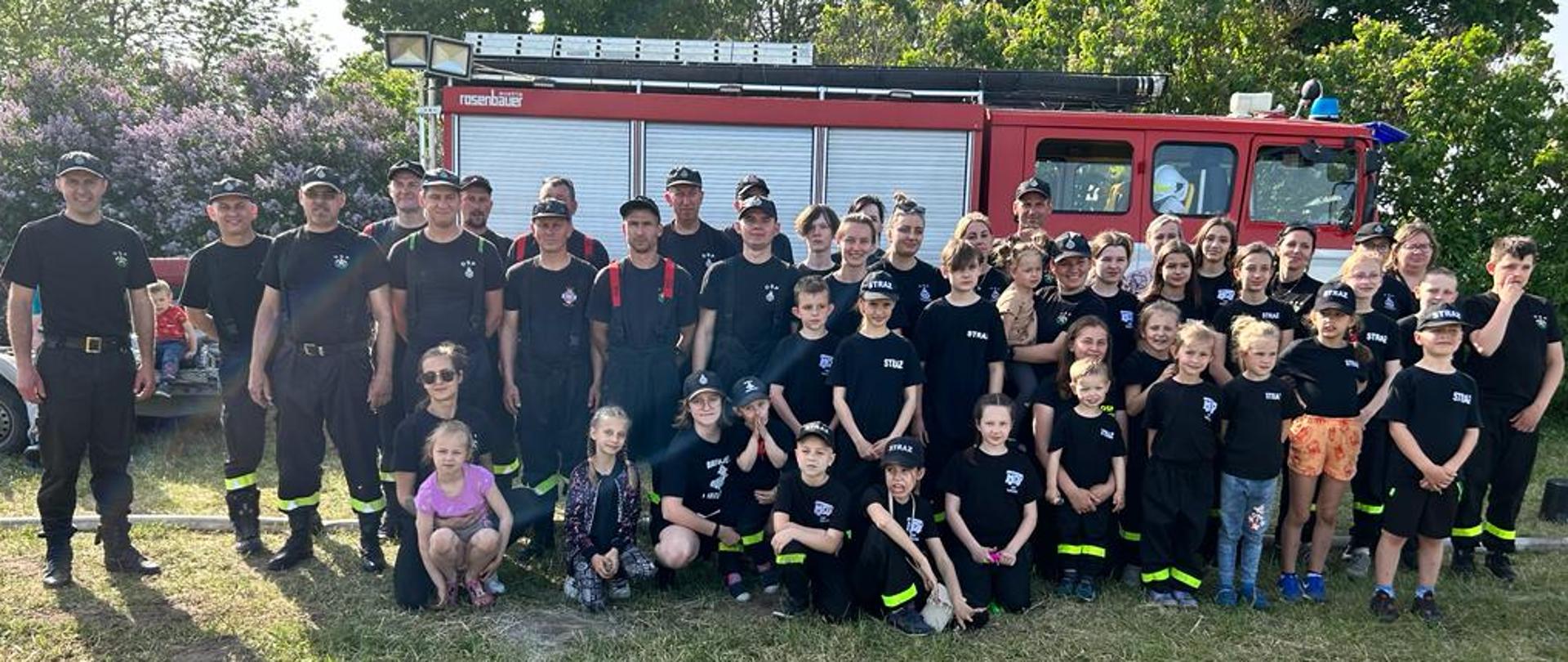 Uczestnicy gminnych zawodów sportowo-pożarniczych Ochotniczych Straży Pożarnych w Bronisławowie pozują do zdjęcia na tle samochodu pożarniczego.